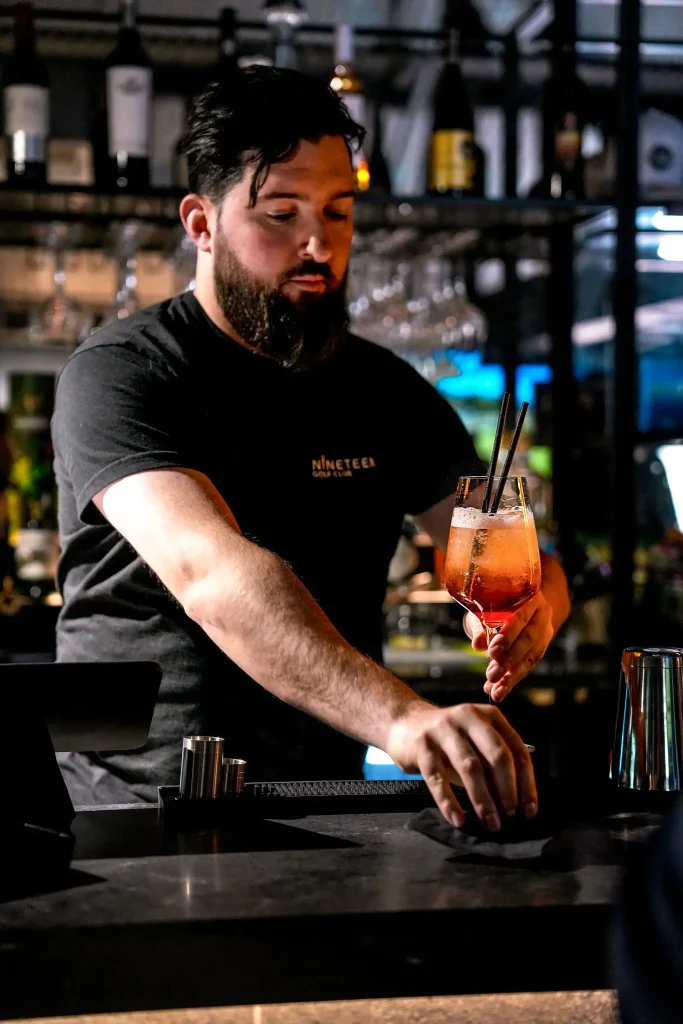 A bar man serving an aperol spritz at the bar